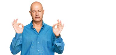 Orta yaşlı kel adam rahat kıyafetler giyiyor ve gözleri kapalı gülümsüyor parmaklarıyla meditasyon hareketi yapıyor. yoga konsepti. 