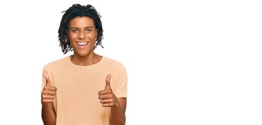 Genç afro-amerikan adam günlük kıyafetler giyiyor başarı işareti yapıyor, elleriyle olumlu jest yapıyor, gülümsüyor ve mutlu. Neşeli ifade ve kazanan jest. 