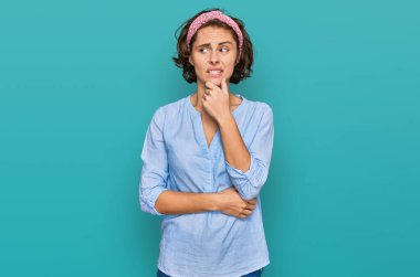 Latin kökenli genç bir kadın gündelik kıyafetler giyiyor ciddi bir yüz ifadesi var eli çenesinde soru soran, kafa karıştırıcı bir fikir hakkında düşünceli. 