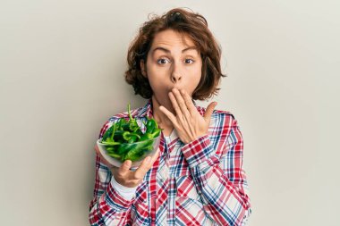 Elinde yeşil biberli kase tutan genç esmer kadın ağızlarını eliyle kapatıyor, şok geçiriyor ve hata yapmaktan korkuyor. şaşırmış ifade 