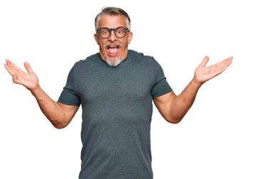 Orta yaşlı, gri saçlı, günlük kıyafetler ve gözlük takan mutlu bir gülümsemeyle zaferi kutlayan ve ellerini kaldırmış bir adam. 