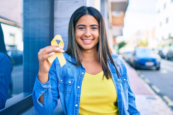 Young latin woman smiling happy holding yellow ribbon at city.