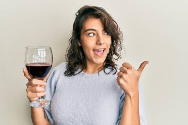 Bir bardak kırmızı şarap içen genç İspanyol kadın başparmağıyla işaret ederek mutlu bir şekilde gülümsüyor. 