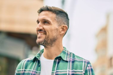 Genç beyaz adam gülümseyerek şehirde mutlu mesut duruyor..
