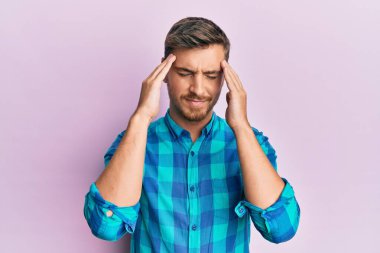 Başı ağrıyan, acı çeken ve migren ağrısı çeken günlük kıyafetler giyen yakışıklı beyaz bir adam. Eller başının üstünde.. 
