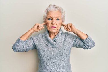 Yaşlı gri saçlı kadın kulaklarını parmaklarıyla kapatıyor. Yüzünde ciddi bir ifade var. Basit ve doğal bir şekilde kameraya bakıyorsun.. 