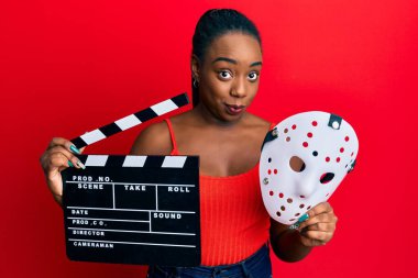 Genç Afro-Amerikan kadın elinde video film panosu ve korku maskesi tutuyor şüpheci ve sinirli, sorun yüzünden surat asıyor. negatif kişi. 