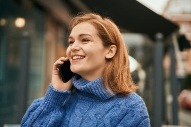 Beyaz kız gülümsüyor. Şehirdeki akıllı telefondan konuşuyor..
