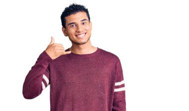 İspanyol asıllı, yakışıklı, sıradan kıyafetler giyen, gülümseyen, el ve parmaklarıyla telefon hareketi yapan, telefonda konuşan genç bir adam. iletişim kavramları. 