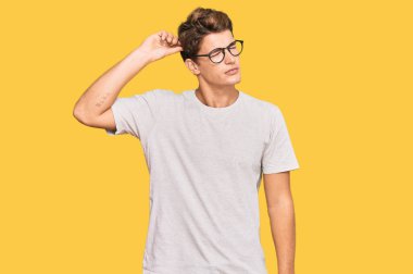 Handsome caucasian man wearing casual clothes and glasses confuse and wondering about question. uncertain with doubt, thinking with hand on head. pensive concept. 