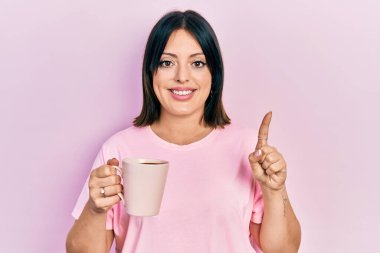 Genç İspanyol kadın bir fincan kahve içip gülümsüyor bir fikirle ya da soru işareti yaparak mutlu bir yüzle, bir numara 