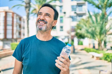 Orta yaşlı, sakallı, mutlu, açık havada su içen bir adam.