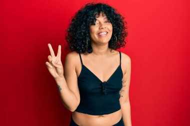 Kolsuz tişörtlü, gündelik giyinen genç İspanyol kadın iki numaralı parmaklarıyla kendini beğenmiş ve mutlu bir şekilde gülümsedi.. 