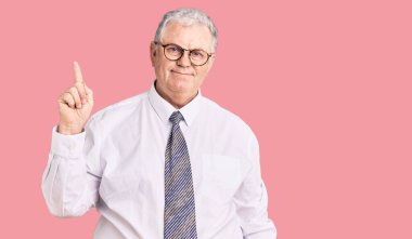 Kıdemli, gri saçlı, iş kıyafetleri giyen, bir numaralı parmağını gösterip, gülümseyen, kendinden emin ve mutlu bir adam.. 