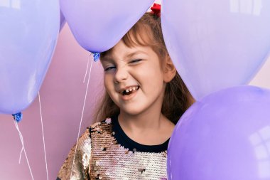 Küçük beyaz kız elinde balonlarla kameraya bakıyor. Seksi bir ifadeyle, neşeli ve mutlu bir yüzle.. 