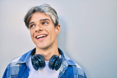 Şehirde kulaklık takarak mutlu gülümseyen genç İspanyol adam..