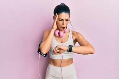 Genç İspanyol kadın spor kıyafetleri giyiyor ve kulaklık takıyor. Saate bakıyor. Endişeli, geç kalmaktan korkuyor. 