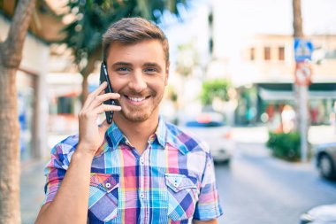 Genç beyaz adam gülümsüyor. Şehirdeki akıllı telefondan konuşuyor..