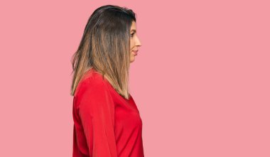 Güzel esmer kadın, günlük giysiler giyip yan tarafa bakıyor, rahat poz veriyor, kendine güvenen bir gülüşü var.. 