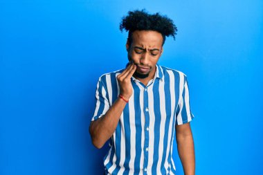 Sakallı, sıradan çizgili tişört giyen, diş ağrısı ya da diş hastalığından dolayı eli ve eli ağrılı bir şekilde ağza dokunan Afro-Amerikalı genç bir adam. dişçi 
