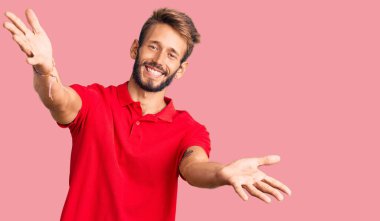 Sarışın, sakallı, sıradan kıyafetler giyen, kameraya bakıp kucaklaşmak için gülümseyen yakışıklı bir adam. Mutluluğu kucaklayan neşeli bir ifade.. 