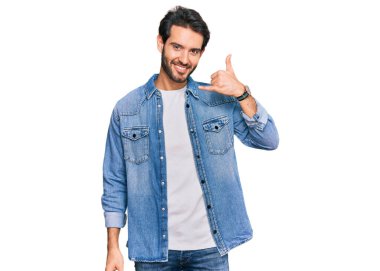 Günlük kıyafetler giymiş, gülümseyen genç İspanyol adam telefonla el ve parmak hareketleri yapıyor telefonda konuşur gibi. iletişim kavramları. 