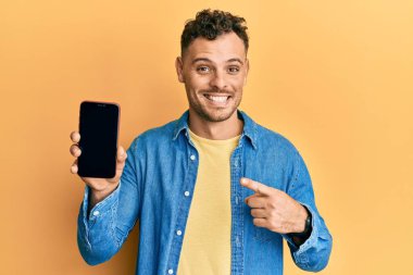 Akıllı telefon tutan genç İspanyol adam boş ekran gösteriyor. Mutluluktan eli ve parmağı işaret ediyor. 