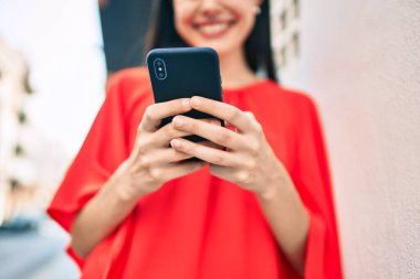 Genç Latin kız şehirde akıllı telefon kullanarak mutlu bir şekilde gülümsüyor..