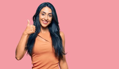 Yazlık elbise giyen güzel İspanyol kadın mutlu ve pozitif gülümsüyor, başparmağıyla mükemmel ve onay işareti yapıyor. 