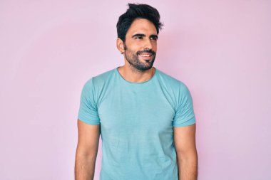 Yakışıklı, sakallı, sıradan kıyafetler giyen, yüzünde gülümseme ve doğal ifadeyle yan yana bakan İspanyol bir adam. Kendinden emin gülen. 