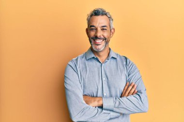 Orta yaşlı, gri saçlı, sıradan kıyafetler giyen mutlu yüzlü, kollarını kavuşturup kameraya bakan bir adam. pozitif kişi. 