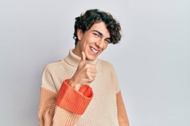 Sıradan bir kazak giyen İspanyol genç adam elleriyle mutlu bir jest yapıyor. Kameraya bakıp başarıyı gösteren ifade. 