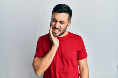 Günlük kıyafetler giyen genç İspanyol adam diş ağrısı ya da diş hastalığından dolayı acı dolu bir ifadeyle ağıza dokunuyor. dişçi 