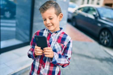 Beyaz çocuk şehirde akıllı telefon kullanarak mutlu bir şekilde gülümsüyor..