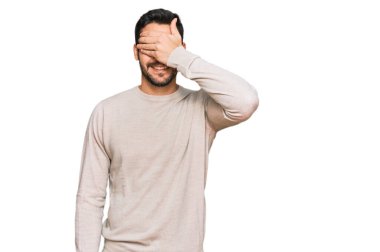 Gündelik kıyafetler giyen, gülümseyen ve gülümseyen genç İspanyol adam şaşırmak için gözlerini kapatıyor. kör kavram. 