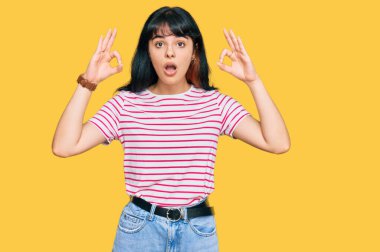 Gündelik kıyafetler giyen genç İspanyol kız şaşırmış ve şok olmuş görünüyor. Tamam sembolünü parmaklarıyla yapıyor. çılgın ifade 
