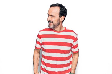Orta yaşlı, çizgili tişört giyen yakışıklı bir adam izole edilmiş beyaz arka planda duruyor. Yan tarafa bakıyor, rahat bir görünüm takınıyor ve kendine güvenen bir gülümseme sergiliyor..
