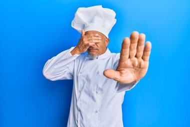Orta yaşlı, gri saçlı, profesyonel aşçı üniforması giyen ve şapkası ellerle gözlerini kapatan üzgün ve korku ifadeleriyle jest yapan bir adam. utangaç ve olumsuz kavram. 