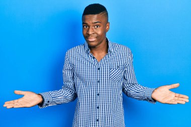 Sıradan kıyafetler giyen, kafası karışmış, elleri ve kolları havada genç Afro-Amerikalı bir adam. şüphe kavramı. 