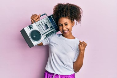 Afro saçlı güzel bir Afrikalı Amerikalı kadın antreman kıyafetleri giyiyor ve elinde müzik kutusuyla gururla haykırıyor, zaferi kutluyor ve başarıyı kollarını kaldırarak kutluyor. 