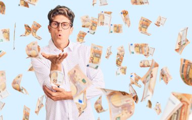 İş kıyafetleri ve gözlük takmış genç yakışıklı bir adam kameraya bakıp havada bir öpücük savuruyor ve sevimli ve seksi oluyor. aşk ifadesi.