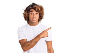Gündelik beyaz tişört giyen genç İspanyol adam endişeli ve gergin bir şekilde işaret ediyor. 
