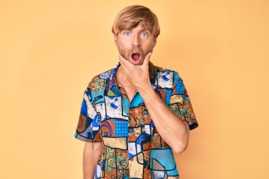 Yazlık gömlek giyen genç sarışın adam, elleri çenesinde, inanamama, şaşkınlık ve şaşkınlık dolu bir ifade takınıyor. 