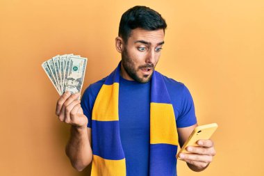 Genç İspanyol futbolcu Amerikan dolarlarını elinde tutan akıllı telefon kullanıyor. Şok olmuş yüzle şüpheci ve alaycı görünüyor. Ağzını açtığında şaşırıyor. 