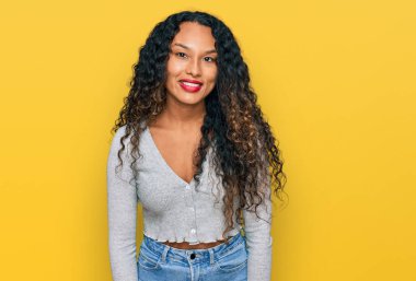 Kıvırcık saçlı, günlük kıyafetler giyen genç İspanyol kadın yüzünde ciddi bir ifadeyle rahatlamış. Basit ve doğal bir şekilde kameraya bakıyorsun.. 