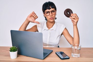Ofiste çalışan güzel bir esmer kadın kızgın suratlı çikolatalı çörek yiyor, olumsuz işaretler baş parmakları aşağıda, reddedilme konsepti ise reddedilmiş. 