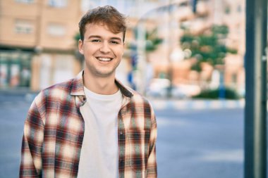 Genç beyaz adam gülümseyerek şehirde mutlu mesut duruyor..