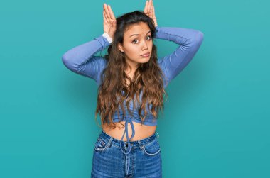 Günlük kıyafetler giyen, tavşan kulağı yapan, avuçlarıyla alaycı ve şüpheci görünen genç İspanyol kız. Paskalya tavşanı konsepti. 