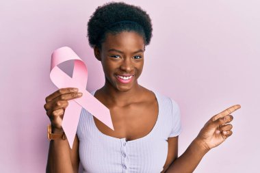 Genç Afro-Amerikalı kız pembe kanser kurdelesi tutuyor gülümsüyor. 