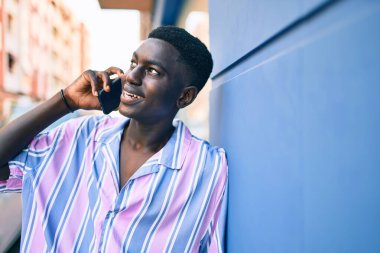 Genç Afrikalı Amerikalı gülümseyen adam şehrin caddesindeki akıllı telefonda mutlu bir şekilde konuşuyor..